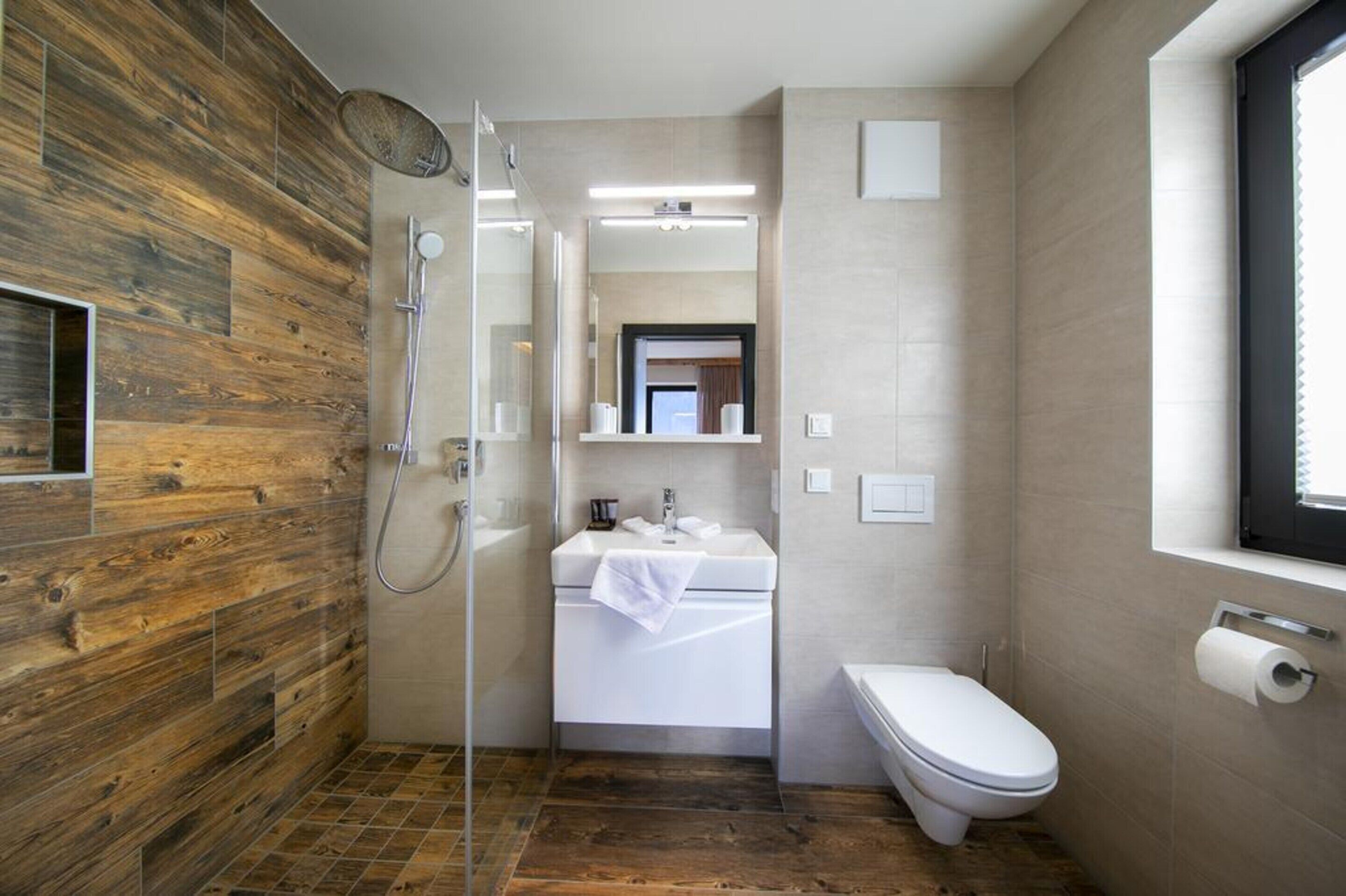 Un bany modern amb una paret de fusta, un cubicle de dutxa amb vidre, un lavabo blanc i un vàter.