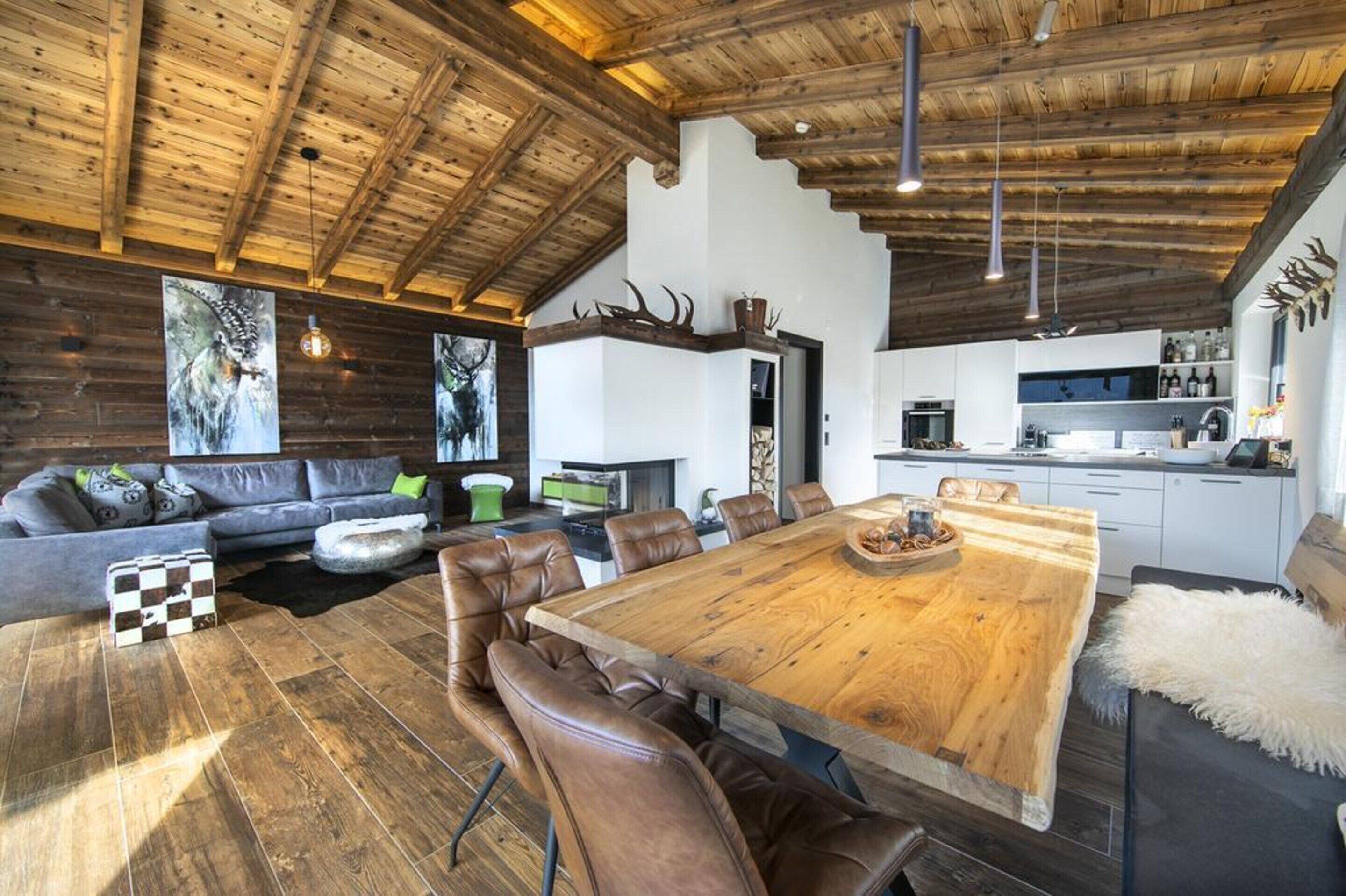 A spacious living area with a large wooden dining table, leather sofas, and a high ceiling with wooden beams.