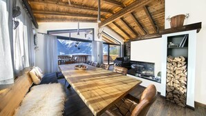 A spacious dining area with a large wooden table, leather seating, and a view of mountains through large windows. - Chalet by the Anfangerpiste Ski-lift (Neukirchen am Grossvenediger)