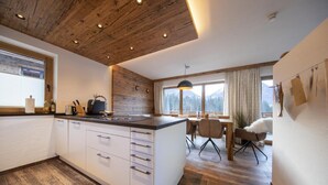A modern kitchen with wooden ceiling, a large island, and a dining area with a view of mountains.