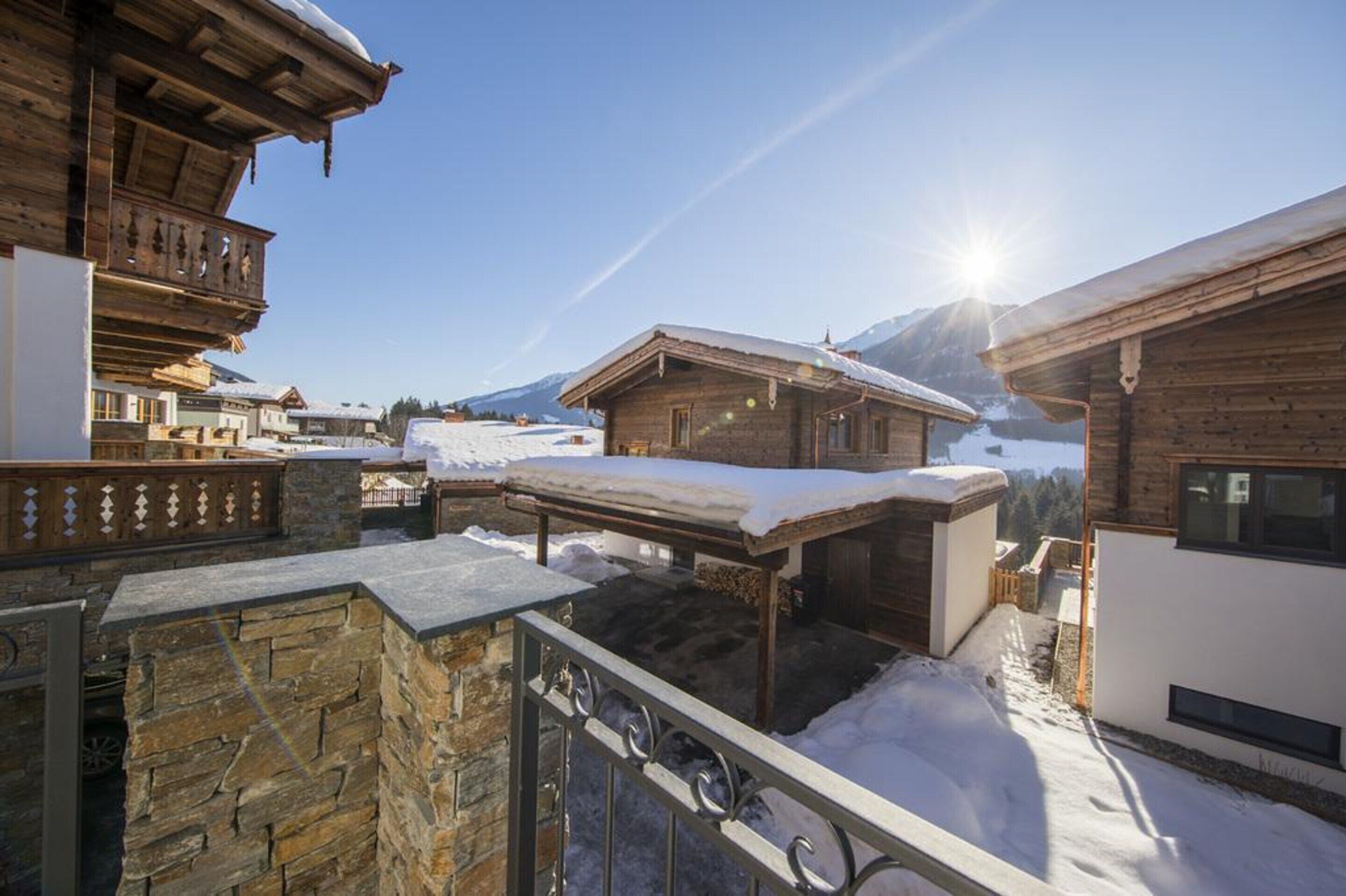 A wooden chalet with a stone facade, a balcony, and a view of a snowy mountain.