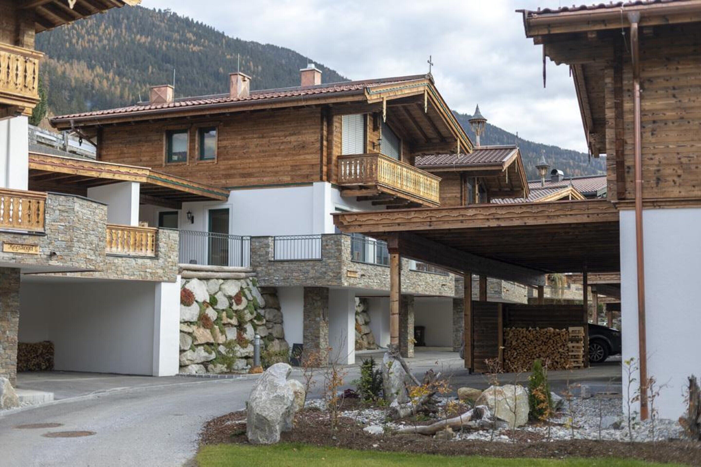 A wooden chalet with stone walls, a balcony, and a covered parking area.