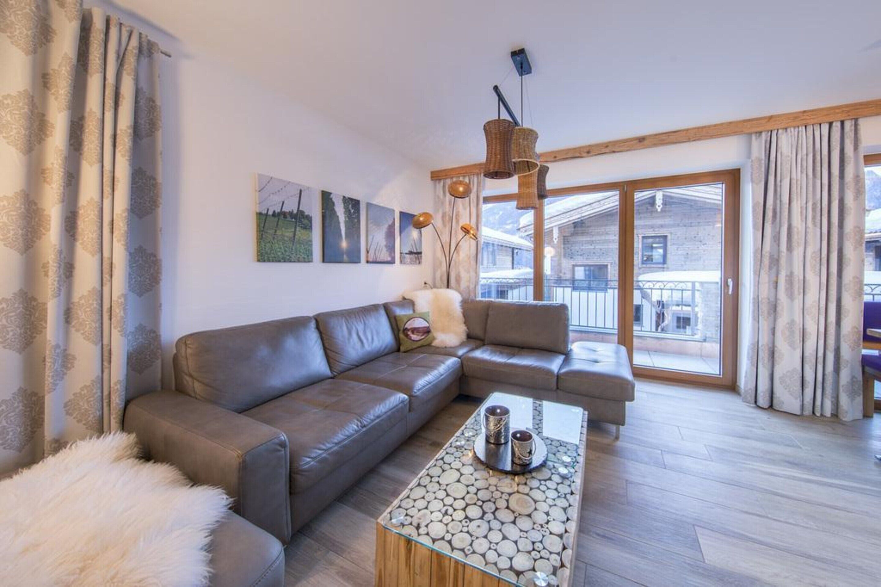 A modern living room with a brown leather sofa, a glass coffee table with decorative elements, and a large window offering a view of a building outside.