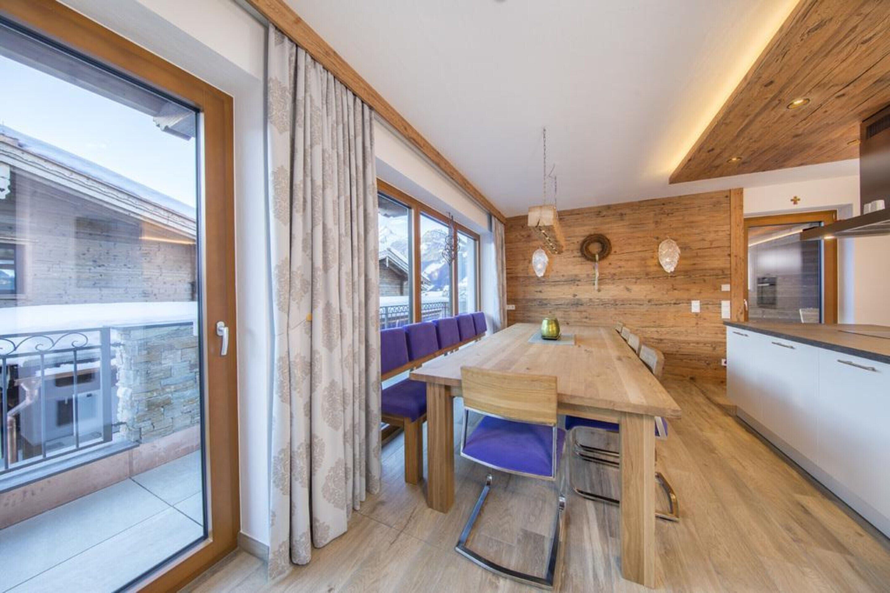 Une cuisine moderne agrémentée d’éléments en bois, un coin repas avec des chaises violettes et une grande fenêtre donnant sur un paysage enneigé.