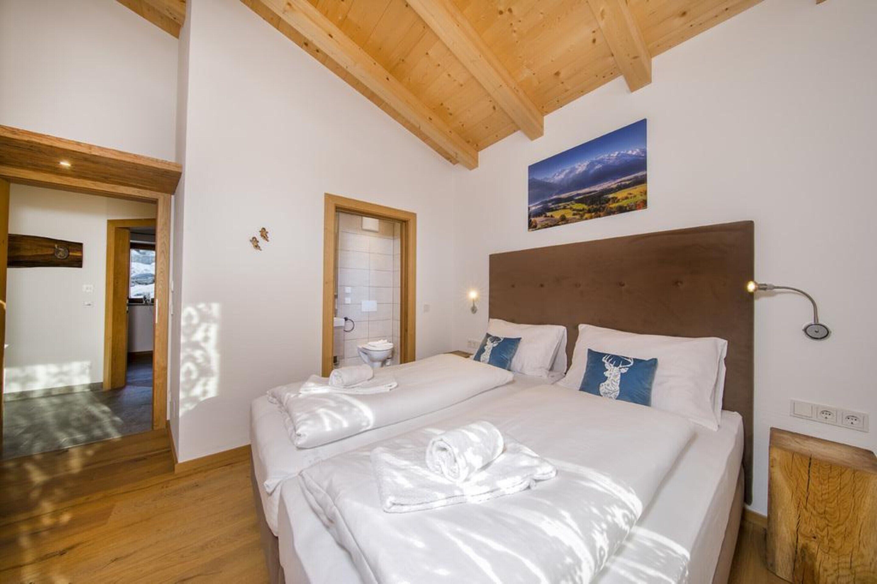 Un dormitorio con dos camas, vigas de madera en el techo, un cuadro de un paisaje y una mesita de noche de madera.