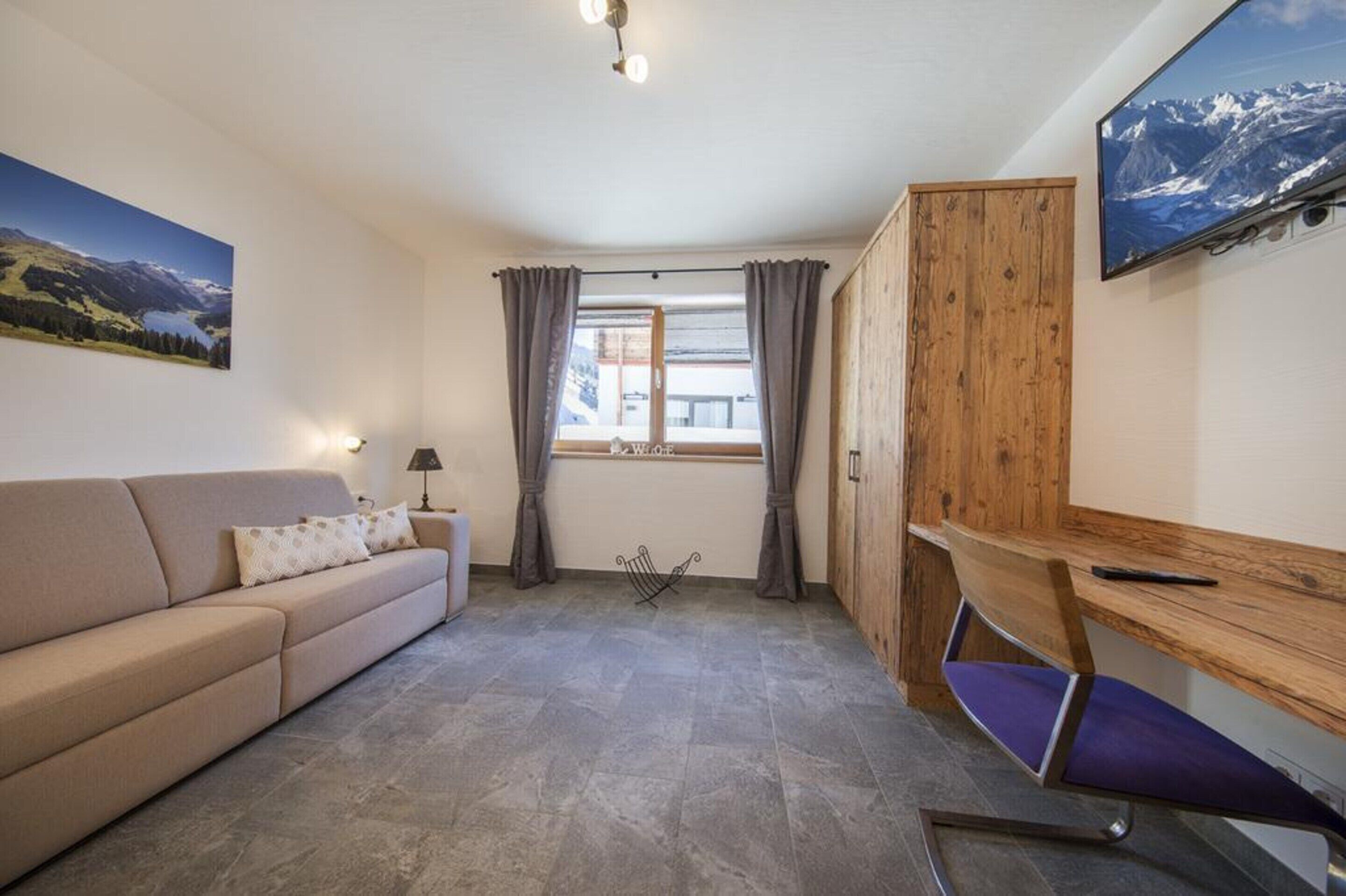 Una habitación acogedora con sofá, escritorio, aparador de madera y ventana con cortinas.