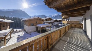Un balcon en bois offrant une vue sur des maisons et des montagnes enneigées.