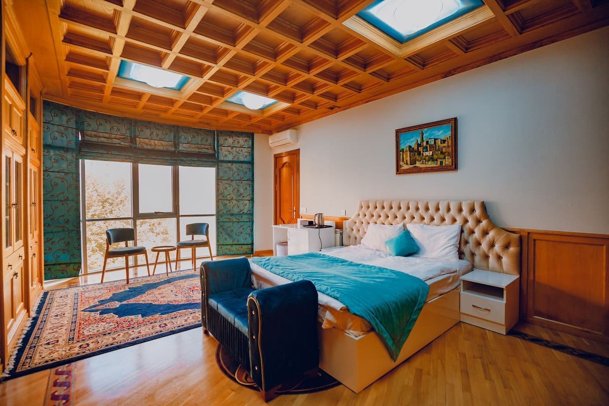A bedroom with a large bed, a desk, a chair, and a window with a view.