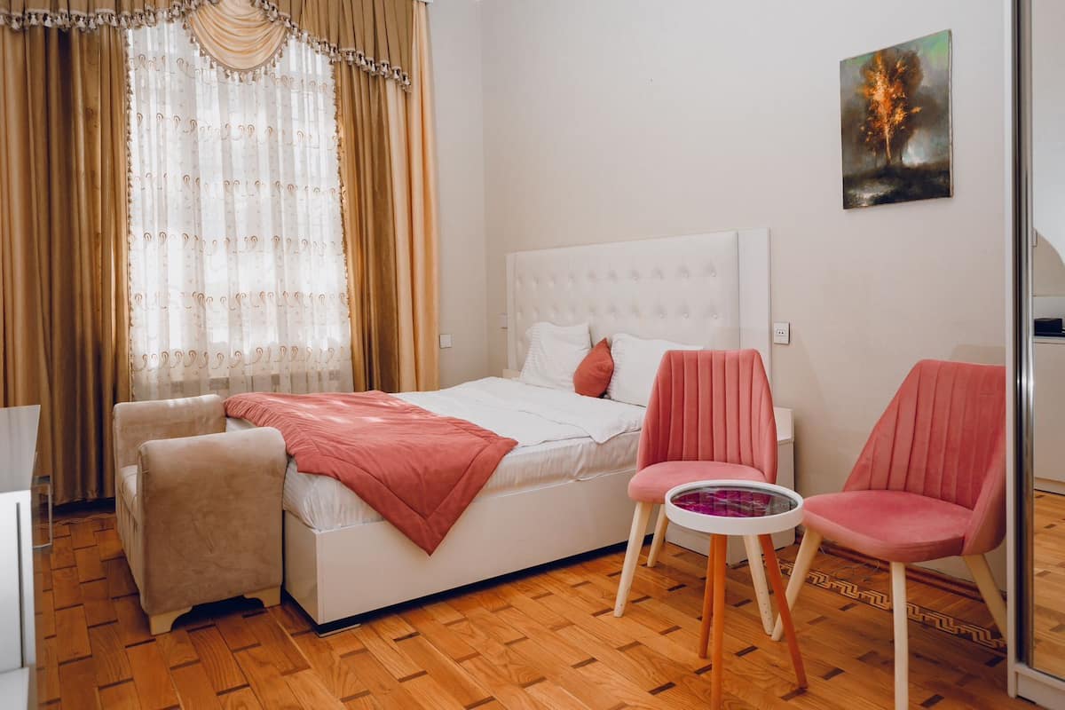 A bedroom with a bed, two chairs, a small table, and a painting on the wall.