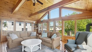 A spacious living room with a large beige sectional sofa, a white coffee table, and a patterned armchair. A ceiling fan and a sign reading "Pine Point" are visible.