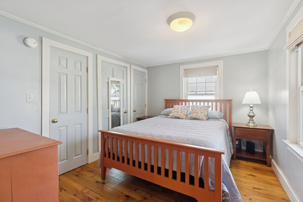 Un dormitorio con una cama de madera, paredes blancas y una ventana con persianas.