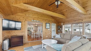 A cozy wooden cabin interior with a large TV, a sofa, and a dining area.