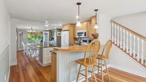A modern kitchen with wooden cabinets, a central island with bar stools, and a view to a dining area.