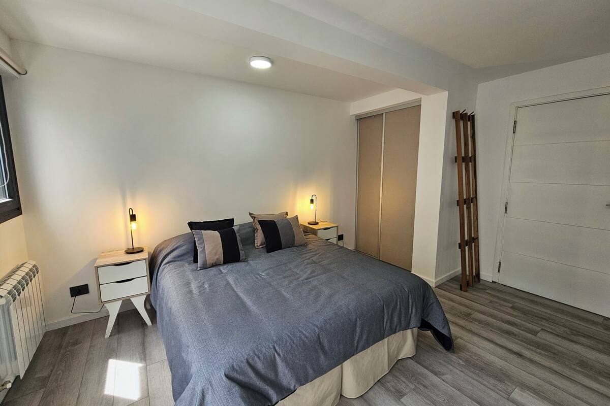 A bedroom with a bed, bedside tables, a radiator, a wardrobe, and a door.