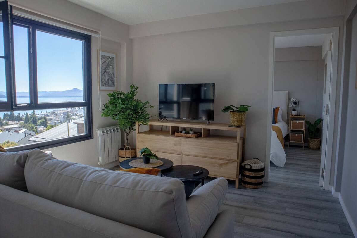 A modern living room with a large window, a flat-screen TV, a sofa, a coffee table, and a wooden cabinet.