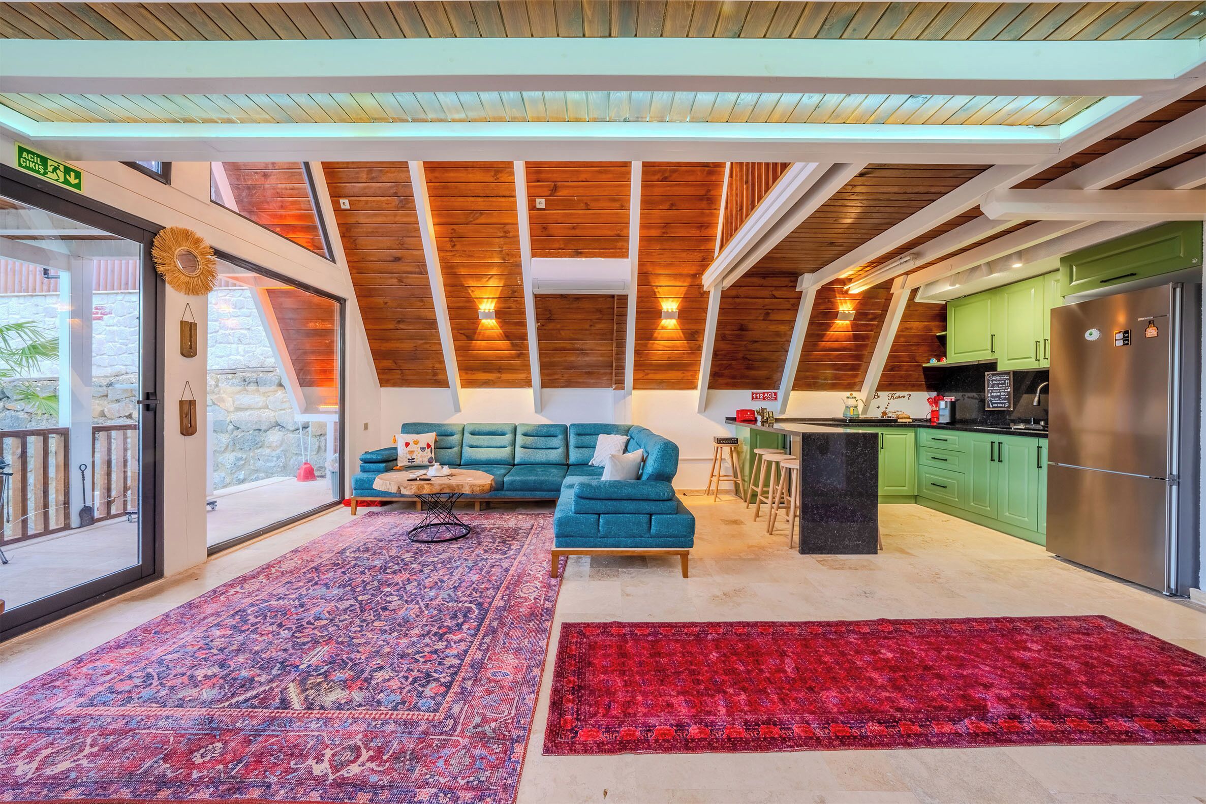 A spacious living area with a blue sofa, a red rug, and a kitchen with green cabinets and a stainless steel refrigerator.
