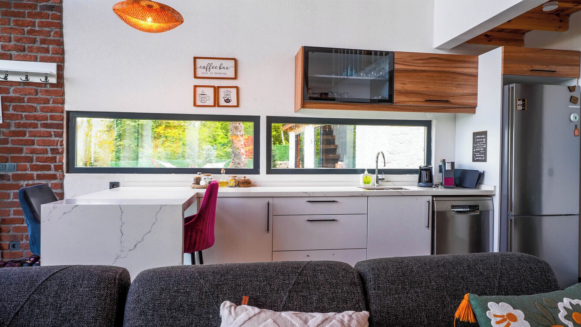 A modern kitchen with a large window, a microwave, and a refrigerator. There are two framed pictures on the wall and a red towel hanging on the door.