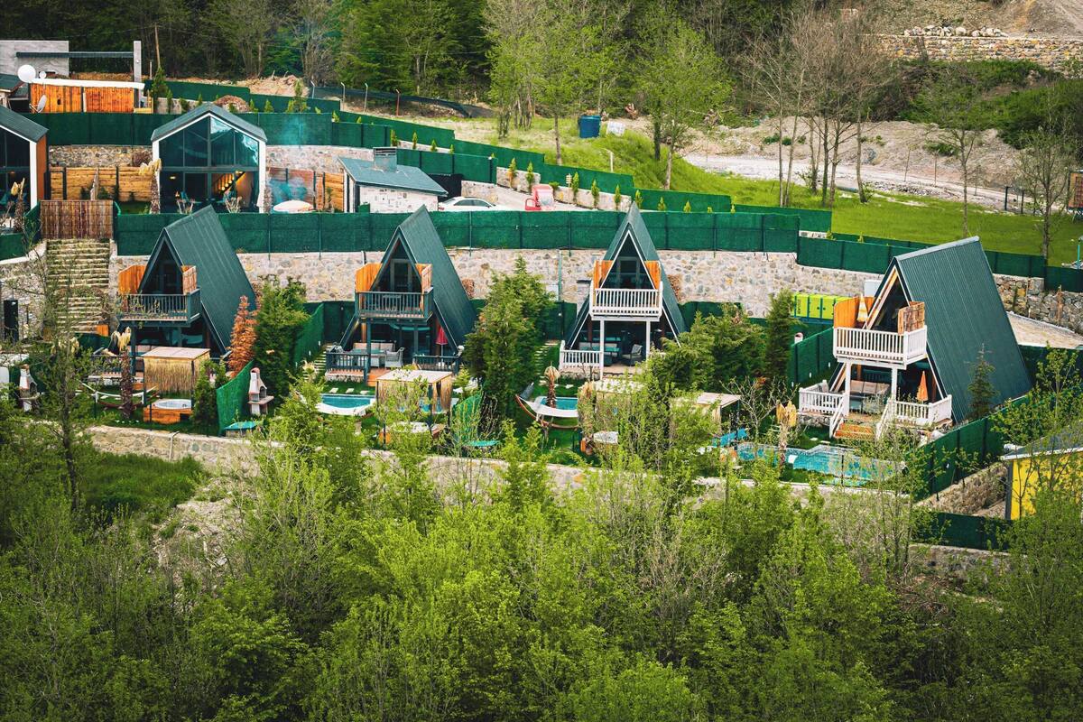 Eine Gruppe von A-Chalets mit Sitzgelegenheiten im Freien, umgeben von viel Grün und einem Schwimmbad.