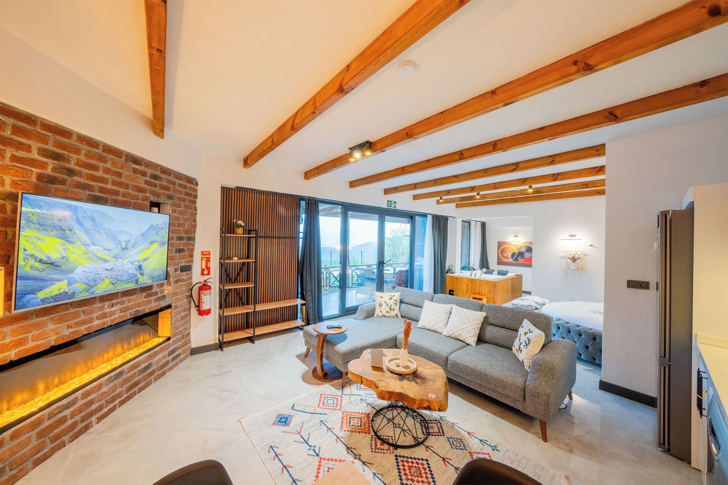 A modern living room with a brick fireplace, a large flat-screen TV, a cozy sofa, and a wooden coffee table.