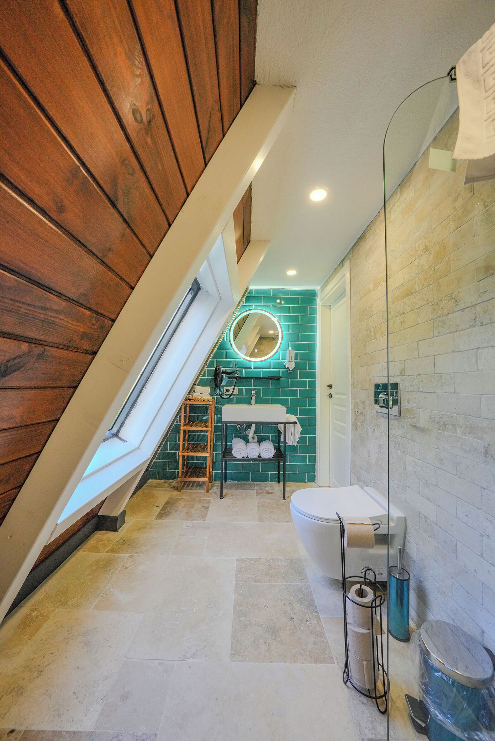 A bathroom with a skylight, a round mirror, a white toilet, and a glass shower enclosure.