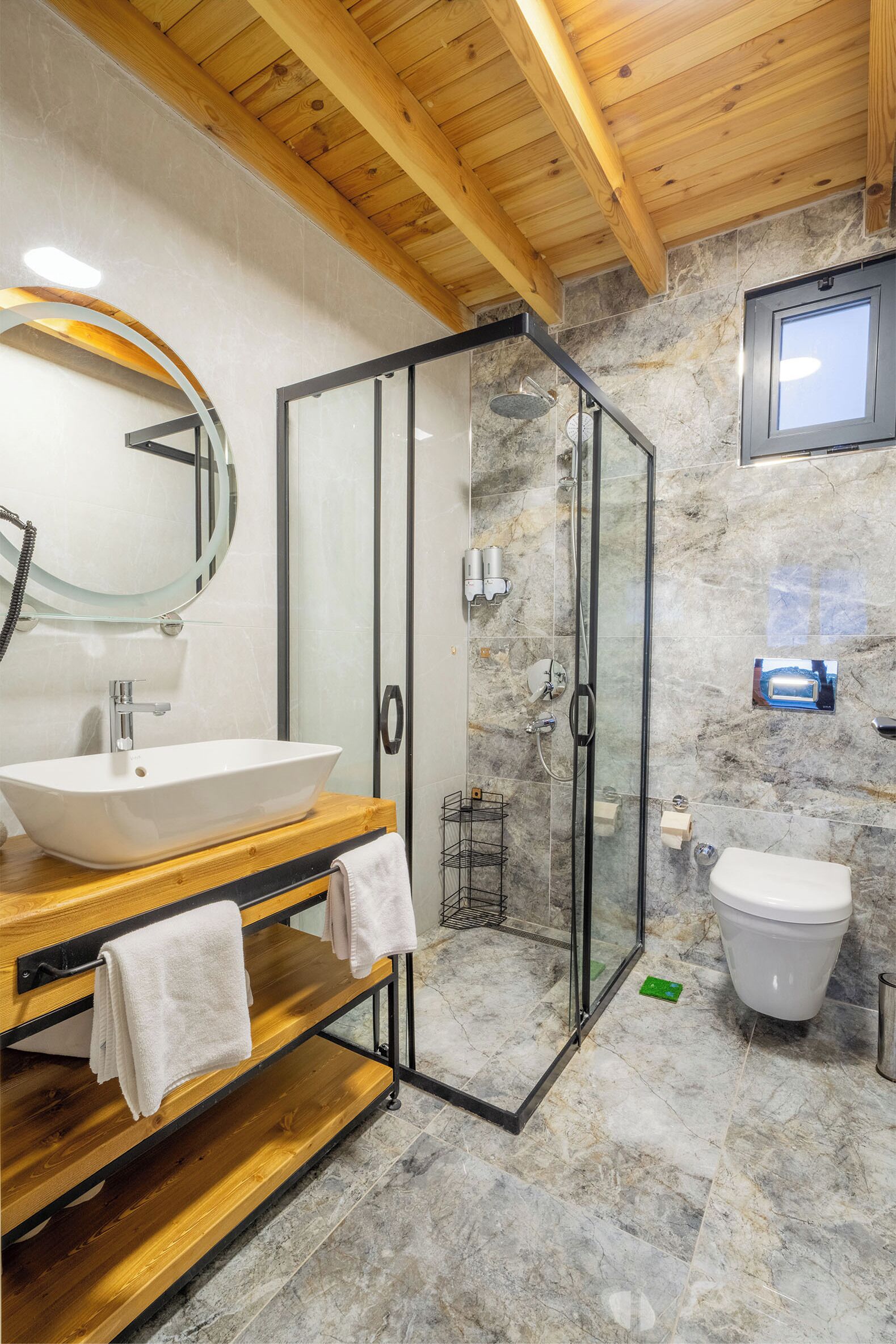 Een moderne badkamer met een houten wastafelmeubel, een douche met glazen wand en een vloer van marmer.