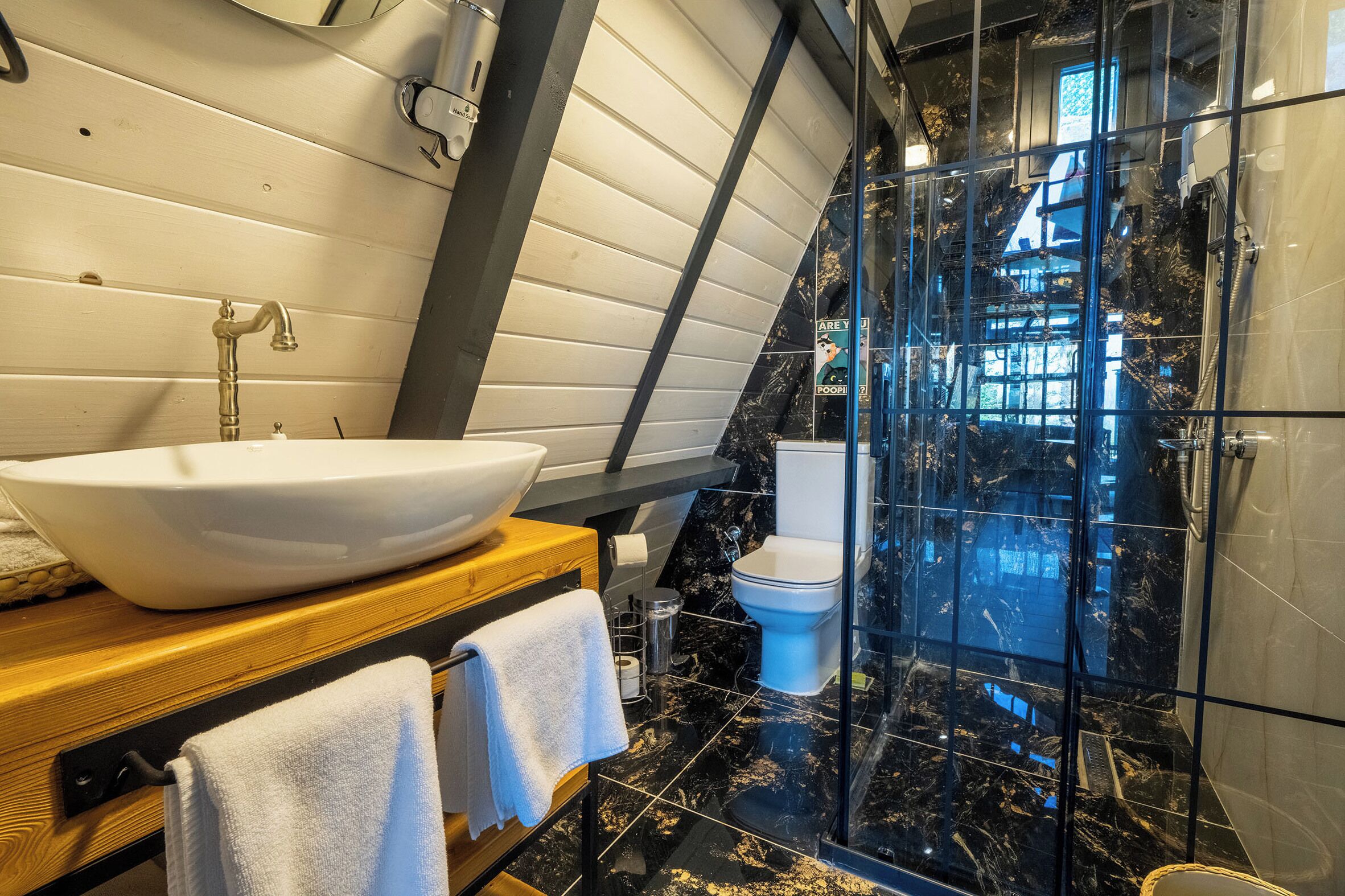 Un baño moderno con un lavamanos blanco de diseño, un mueble de tocador de madera, una ducha con cerramiento de vidrio y un inodoro.