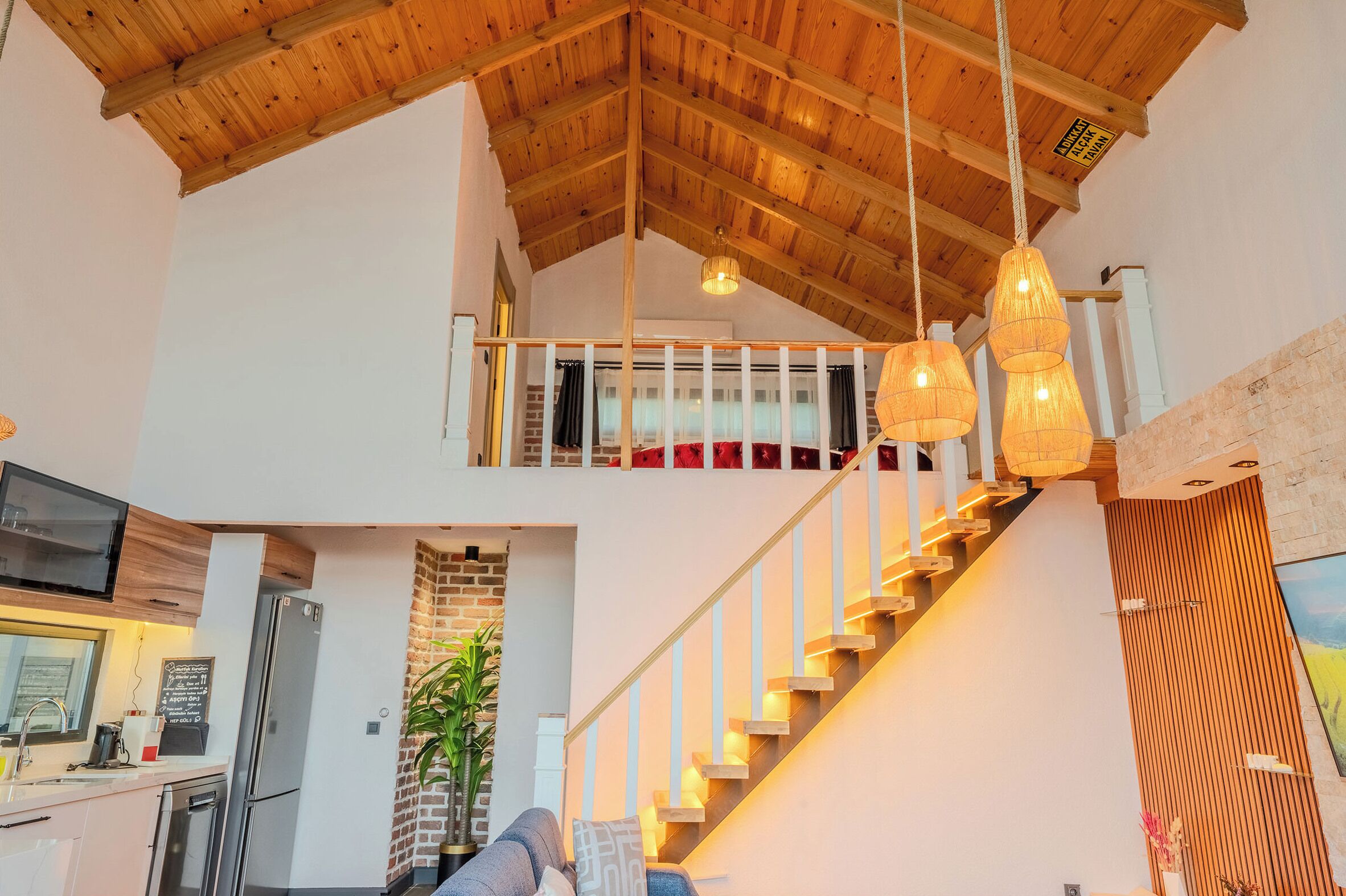 Un interno moderno con soffitto in legno, una scala, un angolo cottura e lampade a sospensione.