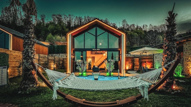 A modern villa with a large glass facade, a pool, and a hammock in the foreground. - Grand Paradise Resort (Sapanca)