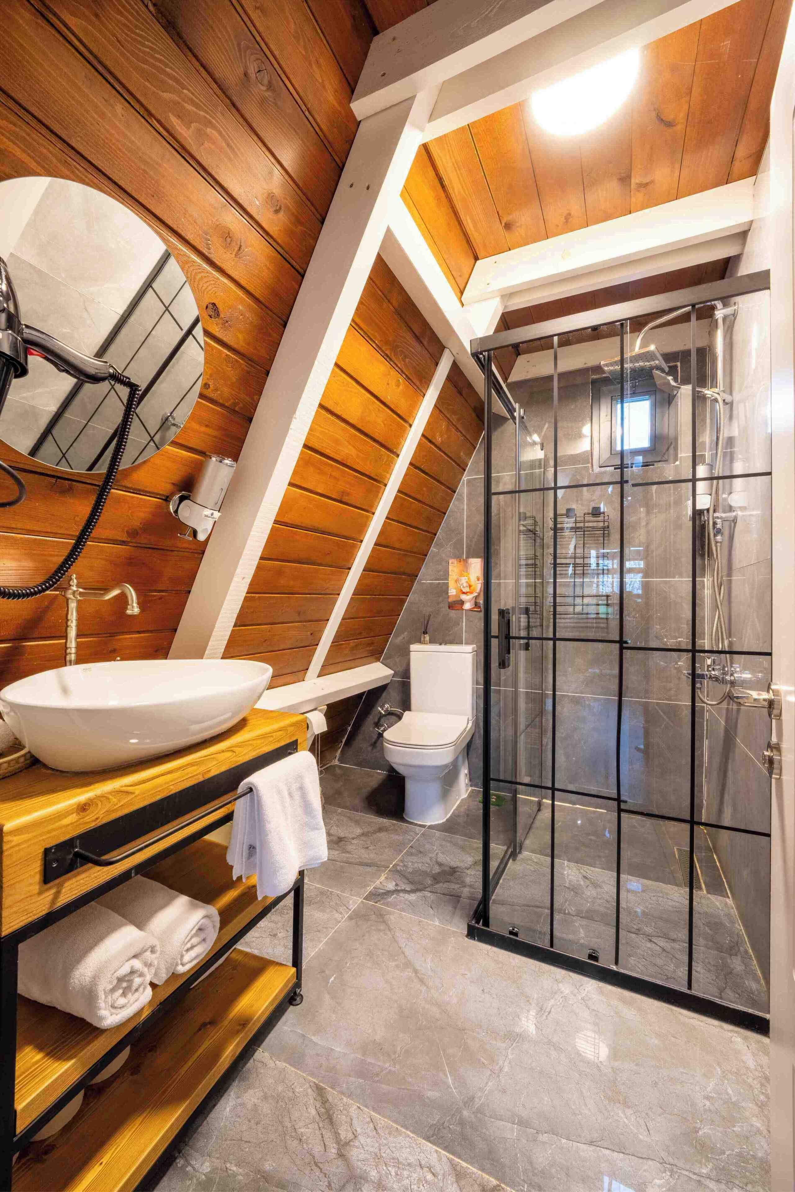 Et moderne badeværelse med træloft, brusekabine i glas, hvid vask og toilet.