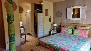 A bedroom with a bed, a nightstand, a wicker bench, a mirror, and a door leading to a bathroom.
