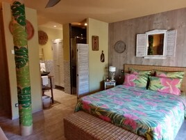 A bedroom with a bed, a nightstand, a wicker bench, a mirror, and a door leading to a bathroom.