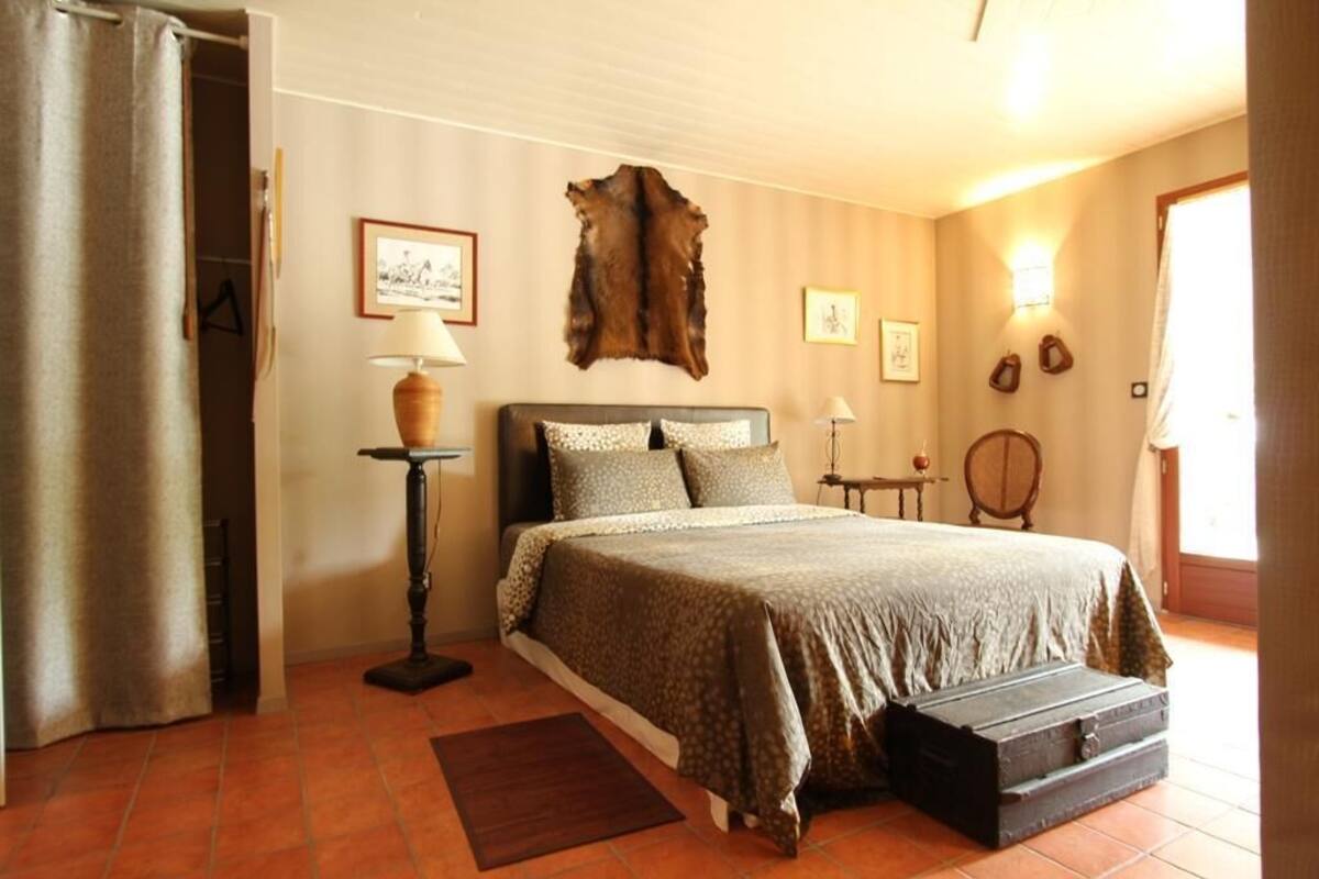Una camera da letto con un letto, un comodino, una lampada, una valigia e un tappeto in pelliccia fissato alla parete.