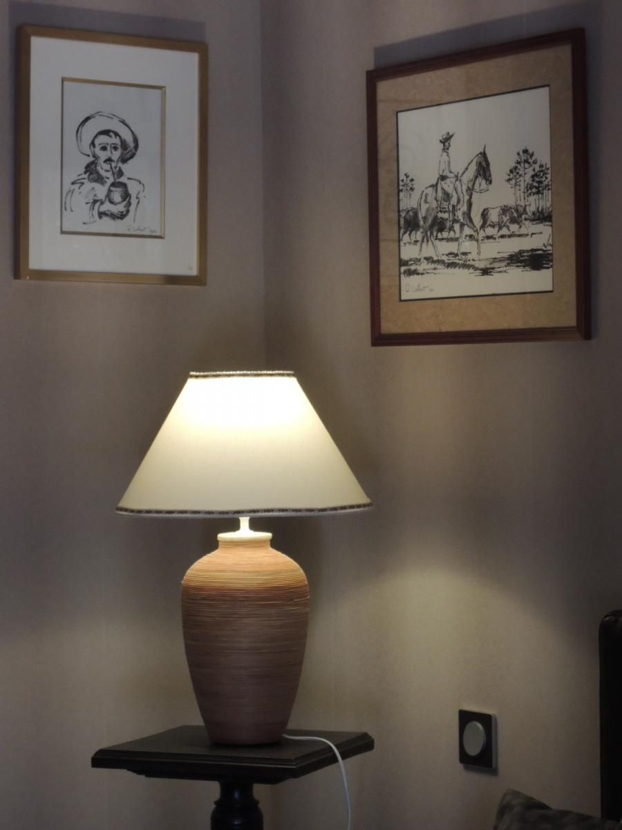 En lampa står på ett bord, och på väggen hänger två inramade konstverk.