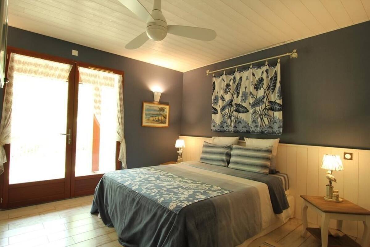 Una camera da letto con un letto, una ventola a soffitto, un comodino con una lampada e una finestra con tende.