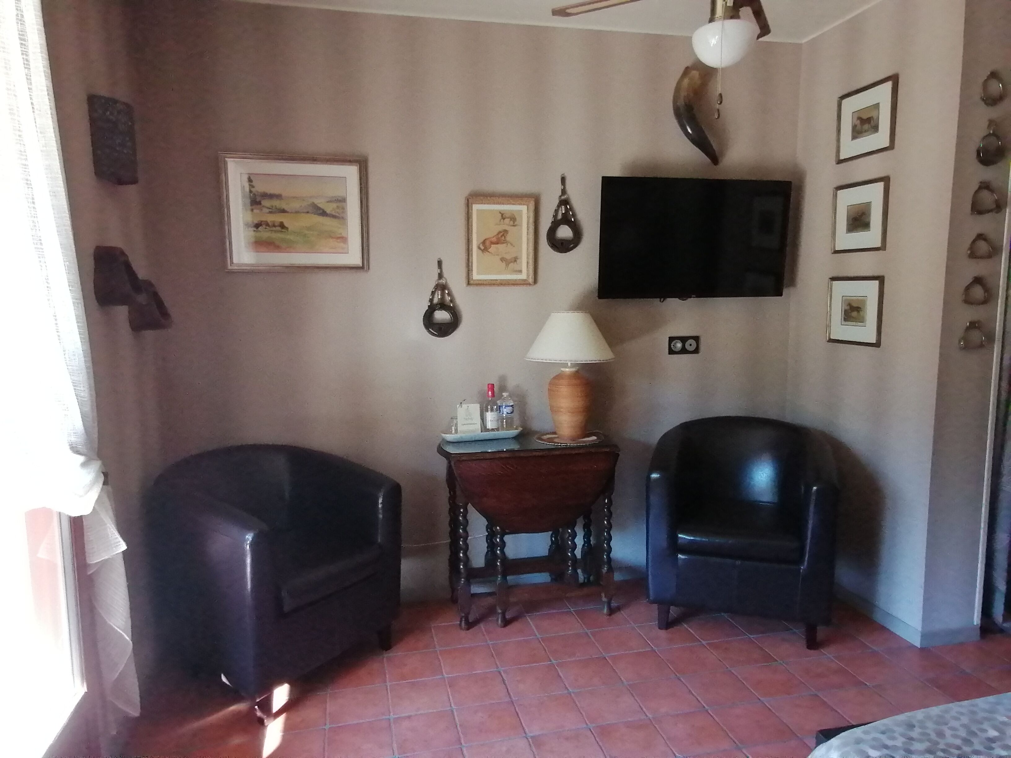A room with two black leather chairs, a wooden side table with a lamp, a flat-screen TV mounted on the wall, and framed pictures.