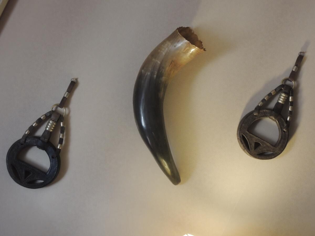 Tres objetos: un cuerno curvado, una pieza metálica circular y un gancho metálico con aro.