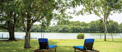Dos sillones con cojines azules en una zona verdejante cerca de un lago, rodeado de árboles.