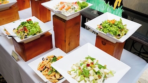A buffet table with various dishes, including salads and pasta, arranged on wooden stands. - Waters Edge Hotel (Battaramulla)