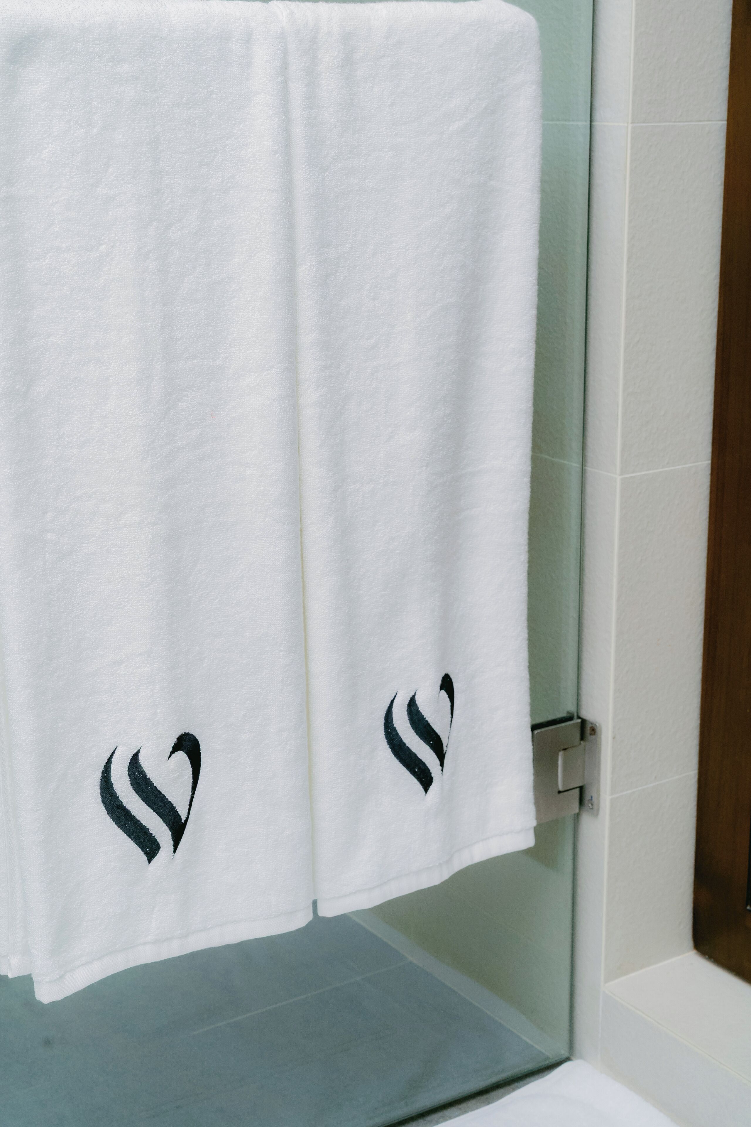 A white towel with a black heart design hanging on a glass shower door.