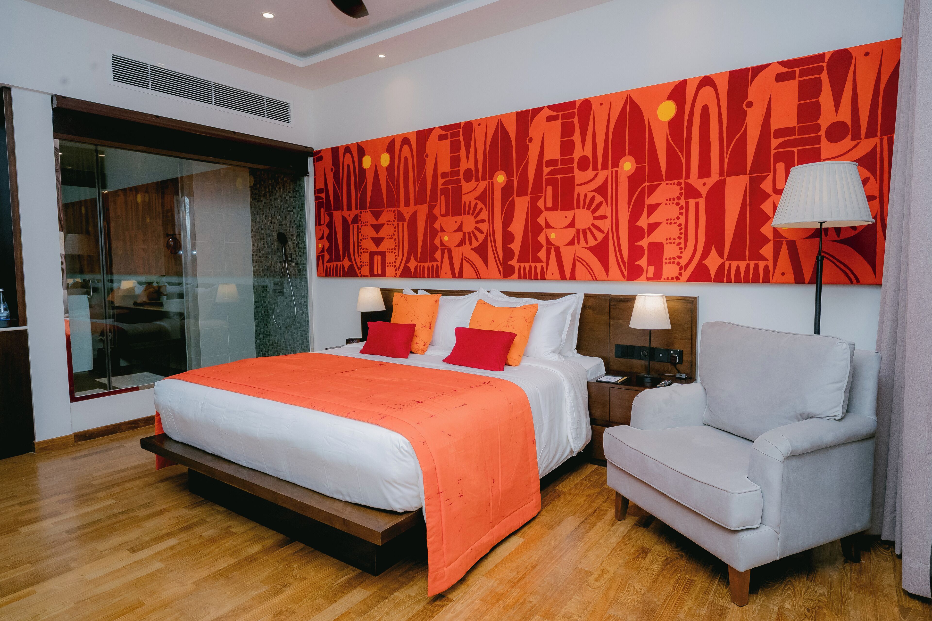 Un dormitorio moderno con una cama grande, un sillón gris, un cuadro abstracto rojo y un ventanal amplio.