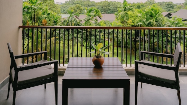 A balcony with two chairs and a table, overlooking a lush green landscape and a body of water. - Waters Edge Hotel (Battaramulla)