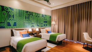 A hotel room with two beds, a ceiling fan, a large abstract painting on the wall, a lamp, and a chair. - Waters Edge Hotel (Battaramulla)