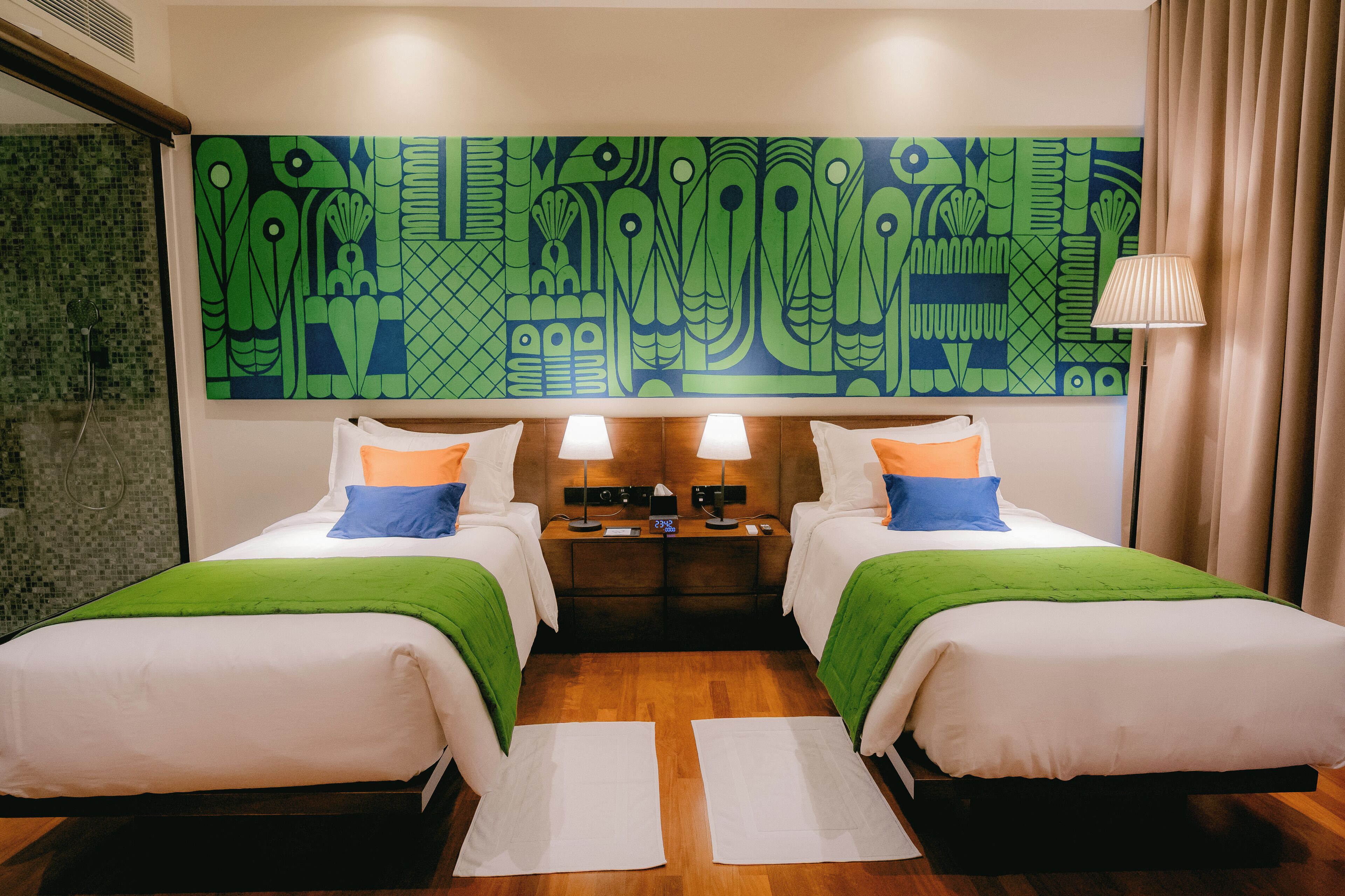 A hotel room with two beds, a large abstract painting on the wall, and a nightstand with lamps.