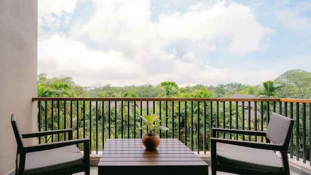 A balcony with two wicker chairs and a table, overlooking a lush green landscape. - Waters Edge Hotel (Battaramulla)
