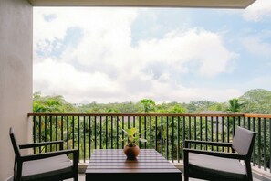 Un balcone con due poltrone in vimini e un tavolo, affacciato su un paesaggio verde e rigoglioso.