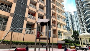 Un terrain de jeux équipé de balançoires et d’une structure d’escalade, entouré de grands immeubles d’habitation.