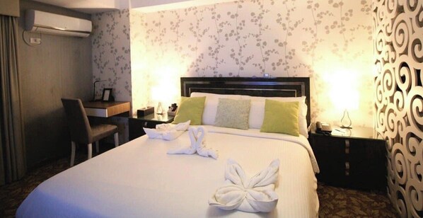 Une chambre d’hôtel avec un lit bien fait, un bureau avec une chaise, une table de chevet avec une lampe et un panneau décoratif au mur.