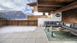 A modern living room with a sofa and coffee table, wooden ceiling, and a view of snow-capped mountains. - Mountain Wellness Stay in Neukirchen (Neukirchen am Grossvenediger)