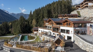 A mountain lodge with a pool, wooden cabins, and a stone wall. - Mountain Wellness Stay in Neukirchen (Neukirchen am Grossvenediger)
