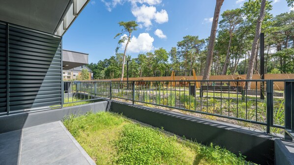 Un bâtiment moderne doté d’une balustrade métallique surplombant un espace paysager agrémenté d’arbres et d’un banc.